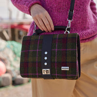 A multicolored tweed handbag with a black leather handle and metal twist clasp, sitting on a mossy surface.