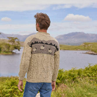 A man standing back view outdoors wearing a beige Aran sweater with a sheep landscape design.