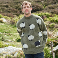 Man wearing a green sweater with sheep pattern standing in a natural landscape.