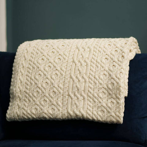 A natural merino aran throw with a geometric pattern draped over a dark-colored sofa cushion.