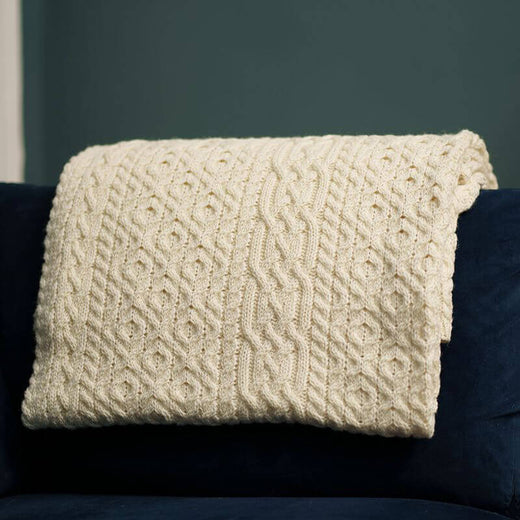 A natural merino aran throw with a geometric pattern draped over a dark-colored sofa cushion.