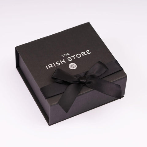 A black gift box from The Irish Store, adorned with a satin ribbon bow on top. The box features the store's logo prominently displayed on the front.
