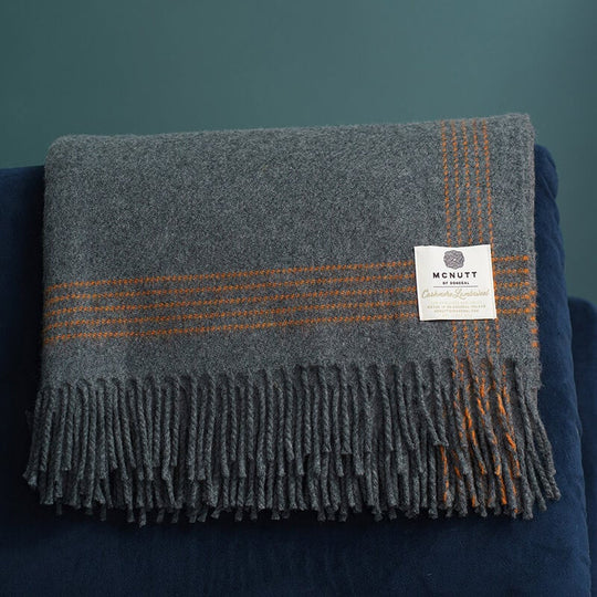 A charcoal Mc Nutt luxury cashmere lambswool throw with orange stripes, displayed on a dark background.