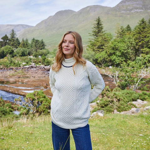 A woman standing outdoors wearing a light-colored aran sweater with a geometric pattern, featuring a crew neck and long sleeves.