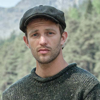 Man wearing a green knitted sweater and an Irish tweed flat cap with a mountainous background