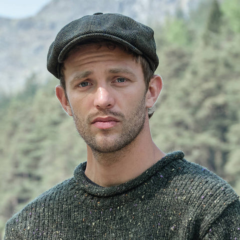 Man wearing a green knitted sweater and an Irish tweed flat cap with a mountainous background