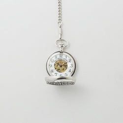 Opened Silver mechanical pocket watch with an engraved Trinity knot design on the cover, hanging from a matching chain against a light background.