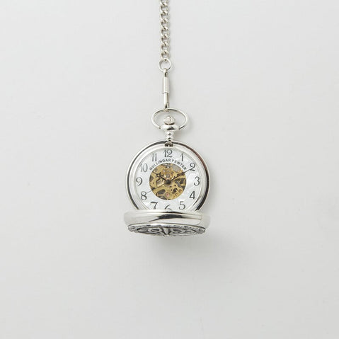 Opened Silver mechanical pocket watch with an engraved Trinity knot design on the cover, hanging from a matching chain against a light background.