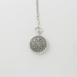 Silver mechanical pocket watch with an engraved Trinity knot design on the cover, hanging from a matching chain against a light background.
