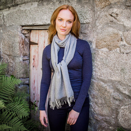 A woman standing in front of a stone wall wearing a gray lambswool scarf with a herringbone pattern.