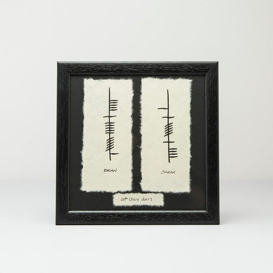 A framed wedding print featuring Ogham script with personalized text and a date, displayed on a white background.