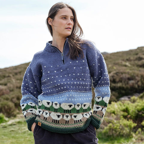 Woman wearing a blue sheep patterned Aran sweater standing in a natural setting