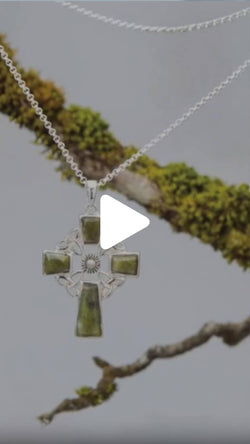 Silver Celtic cross pendant with green marble inlay hanging from a silver chain, displayed against a moss‑covered branch on a light background.