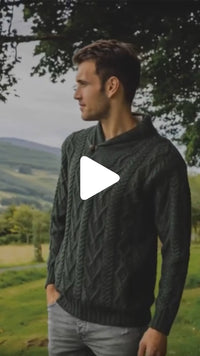 Video of the Men's Classic V-Neck One Button Aran Sweater in dark green, featuring traditional Irish cable knit patterns and a shawl-style collar with a single button, showcased outdoors in a scenic countryside setting.