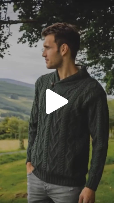 Video of the Men's Classic V-Neck One Button Aran Sweater in dark green, featuring traditional Irish cable knit patterns and a shawl-style collar with a single button, showcased outdoors in a scenic countryside setting.
