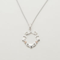 A silver pendant featuring a heart, shamrock, and claddagh design with rose gold accents on a chain.