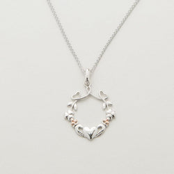 A silver pendant featuring a heart, shamrock, and claddagh design with rose gold accents on a chain.