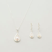 A sterling silver Trinity Knot pendant necklace accompanied by a pair of matching earrings, each featuring a central white pearl, displayed against a light background.