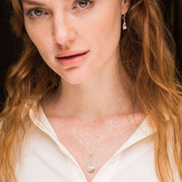 Silver Trinity Knot pearl pendant and matching drop earrings worn by an irish woman with a white collared shirt.