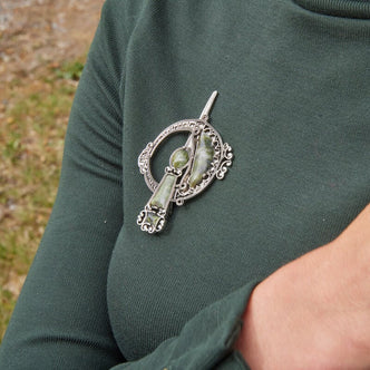 Connemara marble Celtic Tara brooch with intricate silver detailing, pinned to a dark green top outdoors.