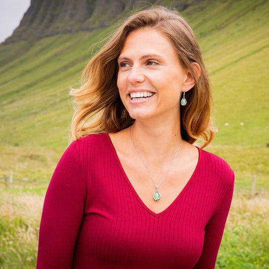 A woman wearing a red v-neck top and showcasing a matching pendant and earrings set with a green cat's eye stone.