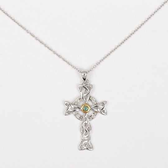 A sterling silver Celtic cross pendant featuring intricate knot work, with a diamond encrusted section and a central sparkling emerald.