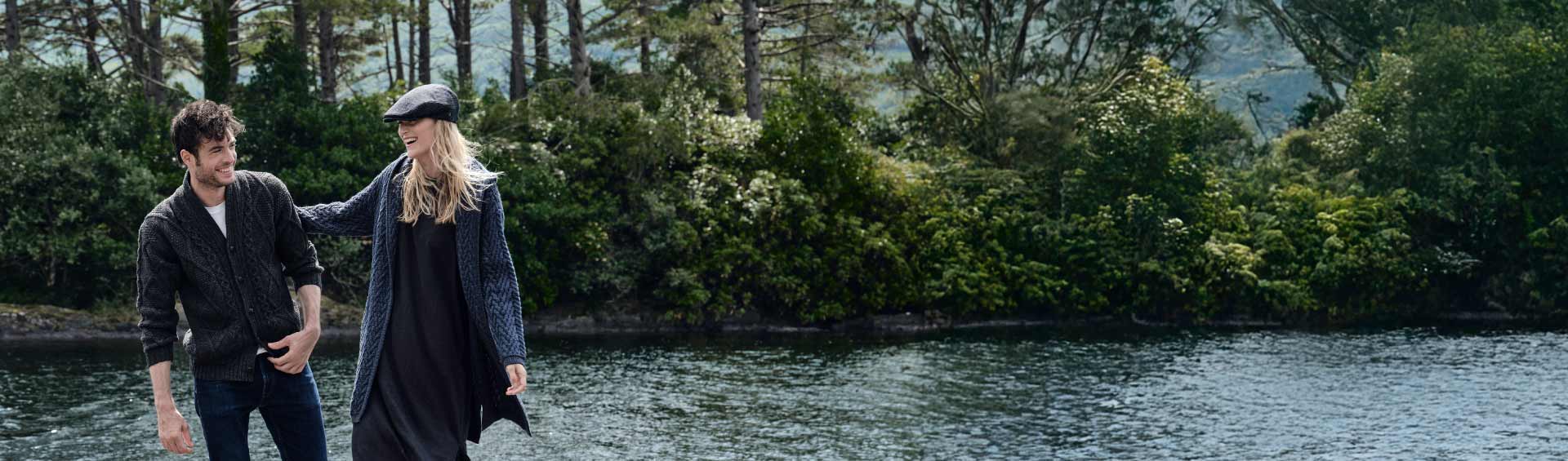 Two people wearing authentic Irish clothings walking by a river with trees in the background
