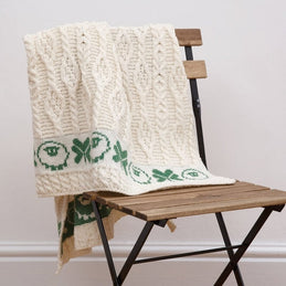 A beige baby blanket with green shamrock and sheep patterns draped over a wooden chair.