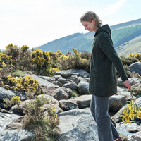 Woman in an army green knitted Aran cardigan standing on rocky terrain with mountains in the background