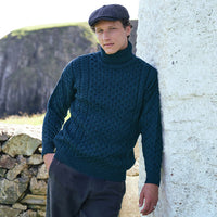 Men's Signature Fisherman Turtleneck Wool Sweater in Blackwatch, crafted from premium wool with traditional Irish Aran stitching and a classic roll neck design, styled beside a traditional stone cottage overlooking the rugged Irish coastline.