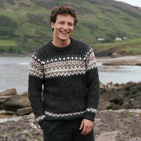 Image featuring the Men's Fairisle Cable Knit Sweater in charcoal, crafted with traditional Fair Isle patterning and authentic Irish cable knit textures, blending heritage-inspired design with timeless knitwear style in a scenic coastal landscape.