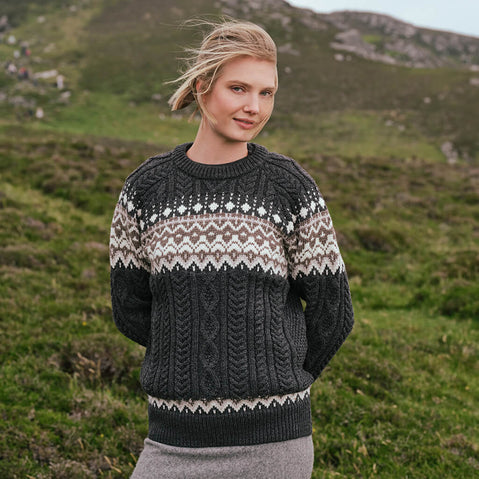 Image featuring the Women's Fairisle Cable Knit Sweater in charcoal, crafted with traditional Fair Isle patterning and authentic Irish cable knit textures, blending heritage-inspired design with timeless knitwear style against a rugged countryside backdrop.