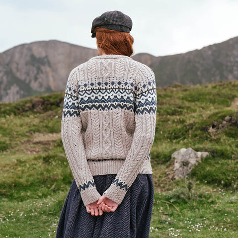 Back view of the Women's Fair Isle Cable Knit Sweater in oatmeal, crafted with authentic cable knit textures and traditional Fair Isle motifs in contrasting tones, showcased against a rugged countryside backdrop inspired by Ireland's natural beauty.