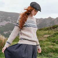 Women's Fair Isle Cable Knit Sweater in oatmeal, crafted with traditional Fair Isle motifs and authentic cable knit textures, showcased from a side view against a scenic Irish mountain landscape.