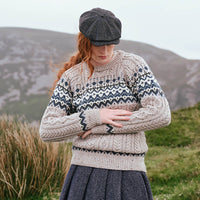 Image featuring the Women's Fairisle Cable Knit Sweater in oatmeal, crafted with traditional Fair Isle patterning and authentic Irish cable knit textures, blending heritage-inspired design with timeless knitwear style against a rugged countryside backdrop.