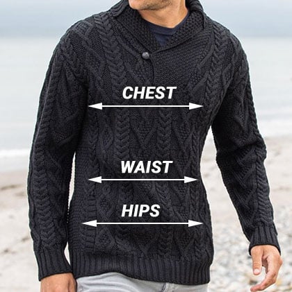 A man wearing a black knitted aran sweater stands on a beach. The image includes labeled arrows indicating 
