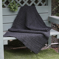 Traditional Aran Honeycomb Wool Throw in charcoal gray yarn draped on a wooden garden bench