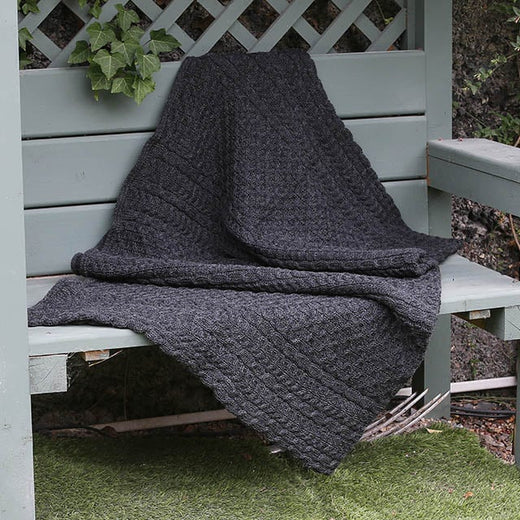 Traditional Aran Honeycomb Wool Throw in charcoal gray yarn draped on a wooden garden bench