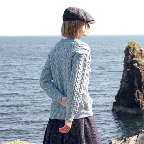 Image featuring the Women's Cable Knit Crew Neck Sweater in light blue, crafted with authentic Irish cable knit patterns and a timeless crew neck silhouette, showcased against a scenic coastal backdrop inspired by Ireland's rugged shoreline.