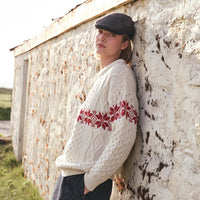 Image featuring the Women's Crew Neck Aran Christmas Sweater in cream, crafted with authentic Irish Aran cable knit textures and a festive red Fair Isle snowflake pattern, combining traditional Irish craftsmanship with timeless holiday style in a scenic countryside setting.