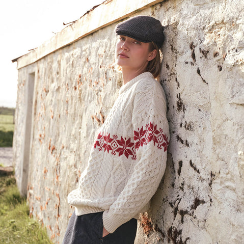 Image featuring the Women's Crew Neck Aran Christmas Sweater in cream, crafted with authentic Irish Aran cable knit textures and a festive red Fair Isle snowflake pattern, combining traditional Irish craftsmanship with timeless holiday style in a scenic countryside setting.