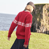 Back view of the Women's Crew Neck Aran Christmas Sweater in red, crafted with authentic Irish Aran cable knit textures and a festive white Fair Isle snowflake pattern, showcasing timeless Irish craftsmanship and classic holiday style in a scenic coastal setting.