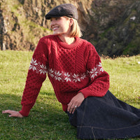 Side view of the Women's Crew Neck Aran Christmas Sweater in red, crafted with authentic Irish Aran cable knit textures and a festive white Fair Isle snowflake pattern, blending traditional Irish craftsmanship with timeless holiday style in a scenic coastal setting.